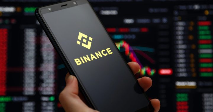 BInance logo on a smartphone, with Binance platform's trading charts in the background